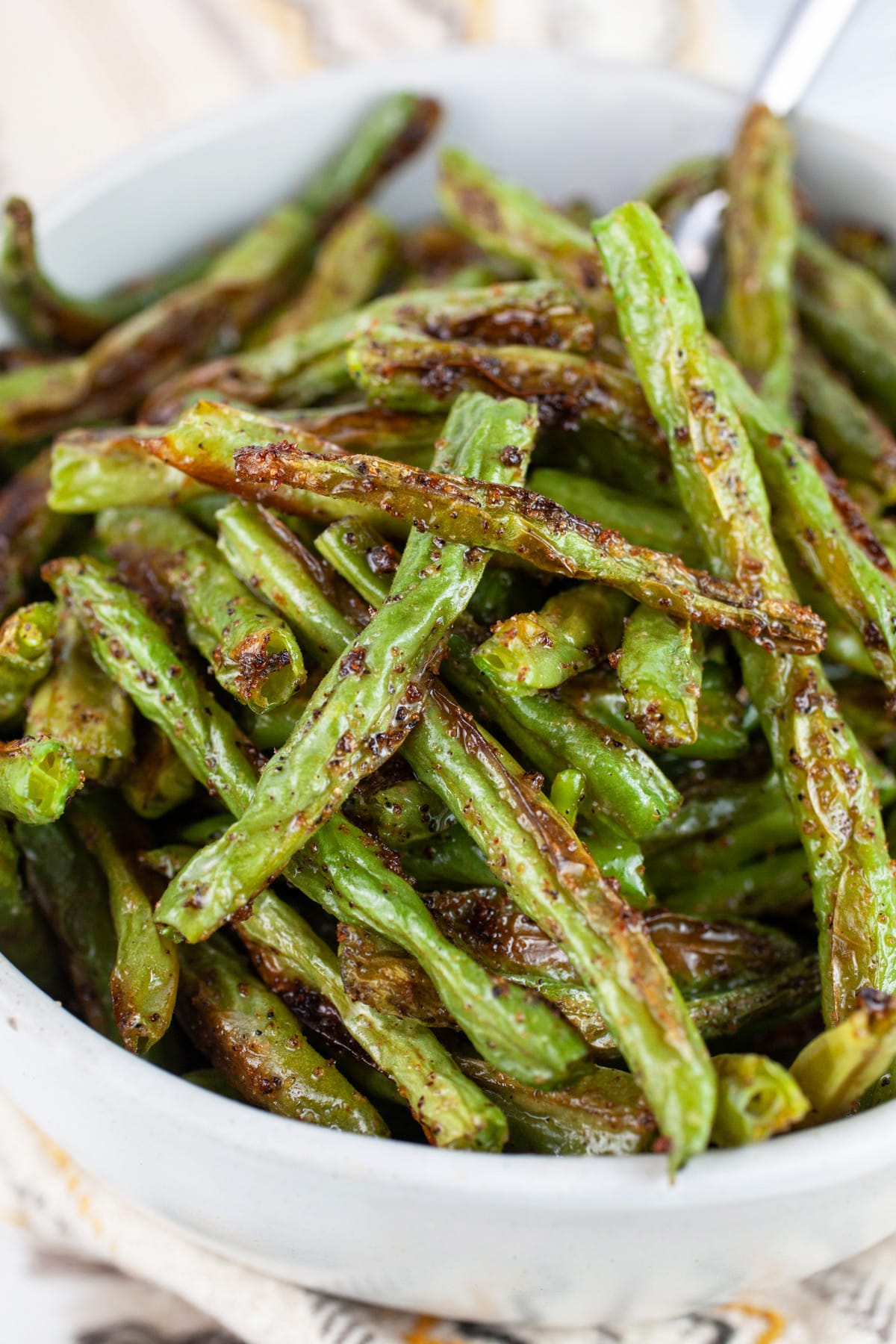Roasted green beans in white bowl with spoon.