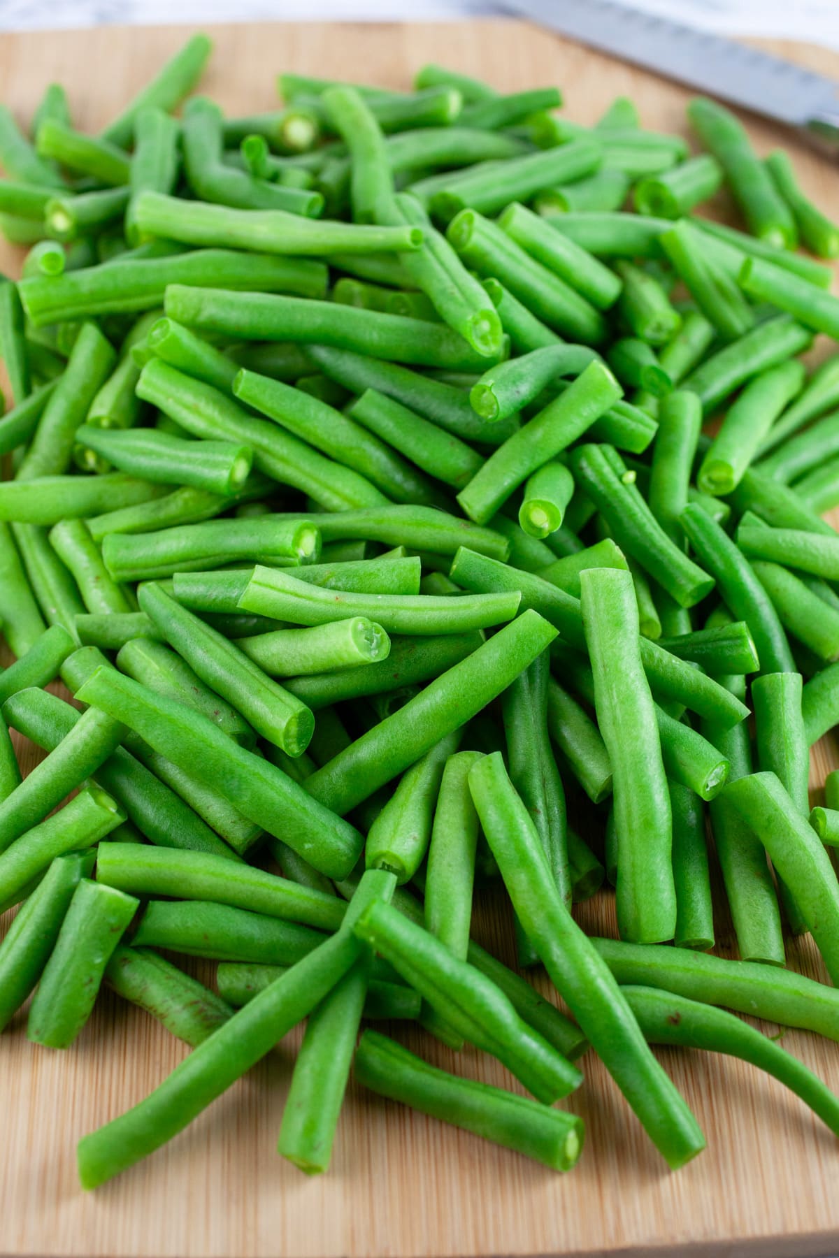 These Simple Garlicky Roasted Green Beans is one of the best easy and healthy side dishes out there! Fresh green beans are tossed in olive oil and garlic powder and then baked in the oven until nice and crispy and then topped with almonds. This quick vegetarian and vegan recipe is perfect for lunch or dinner! #greenbeans #vegetarian #vegan #garlic #withalmonds #easy Fresh chopped green beans on wooden cutting board with knife.
