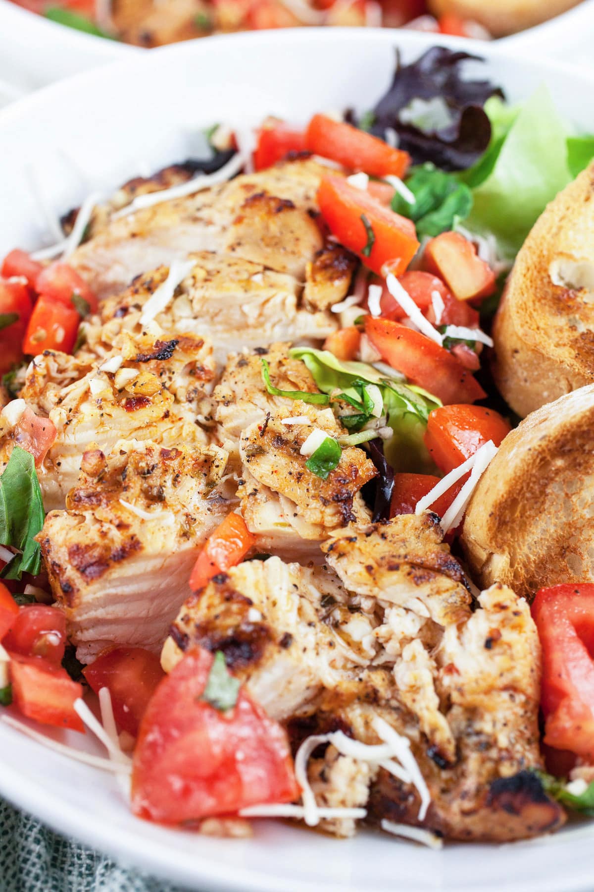 Grilled chicken breasts with tomato basil bruschetta topping and toasted crostini in white bowl.