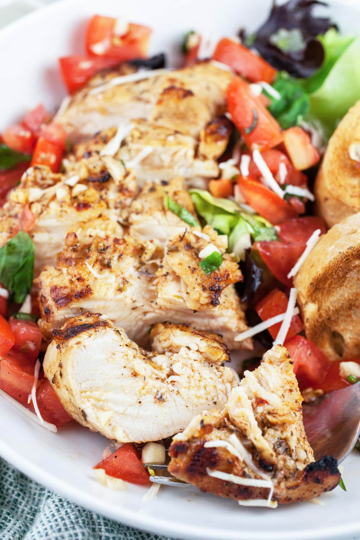 Sliced grilled chicken breasts with tomato bruschetta topping and toasted crostini in white bowl.