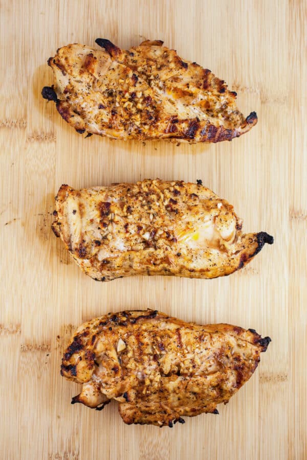 Grilled chicken breasts on wooden cutting board.