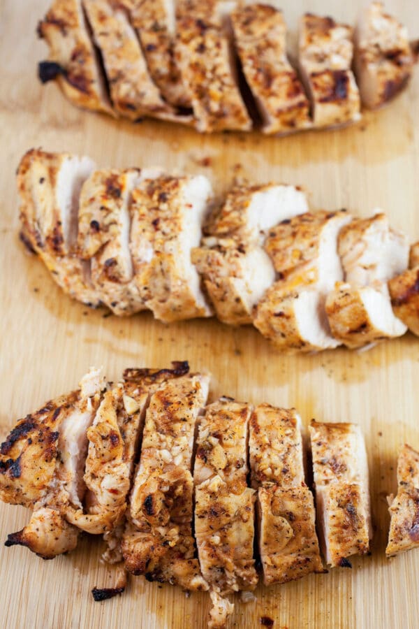 Grilled chicken breasts cut into slices on wooden cutting board.