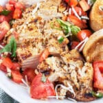 Grilled chicken breasts with tomato bruschetta topping and toasted crostini in white bowl.