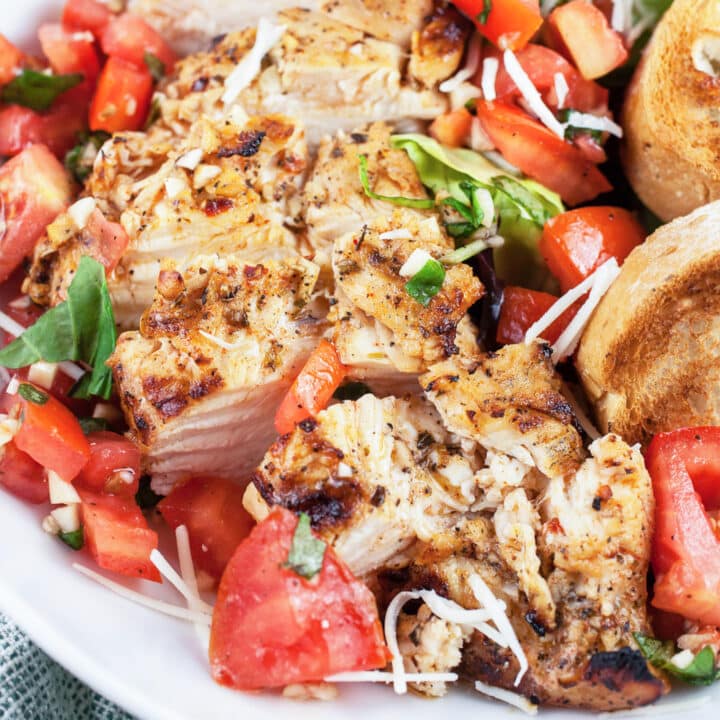Grilled chicken breasts with tomato bruschetta topping and toasted crostini in white bowl.