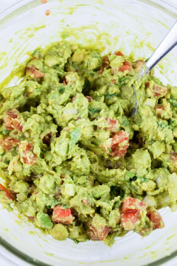 Guacamole mixed in glass bowl with spoon.