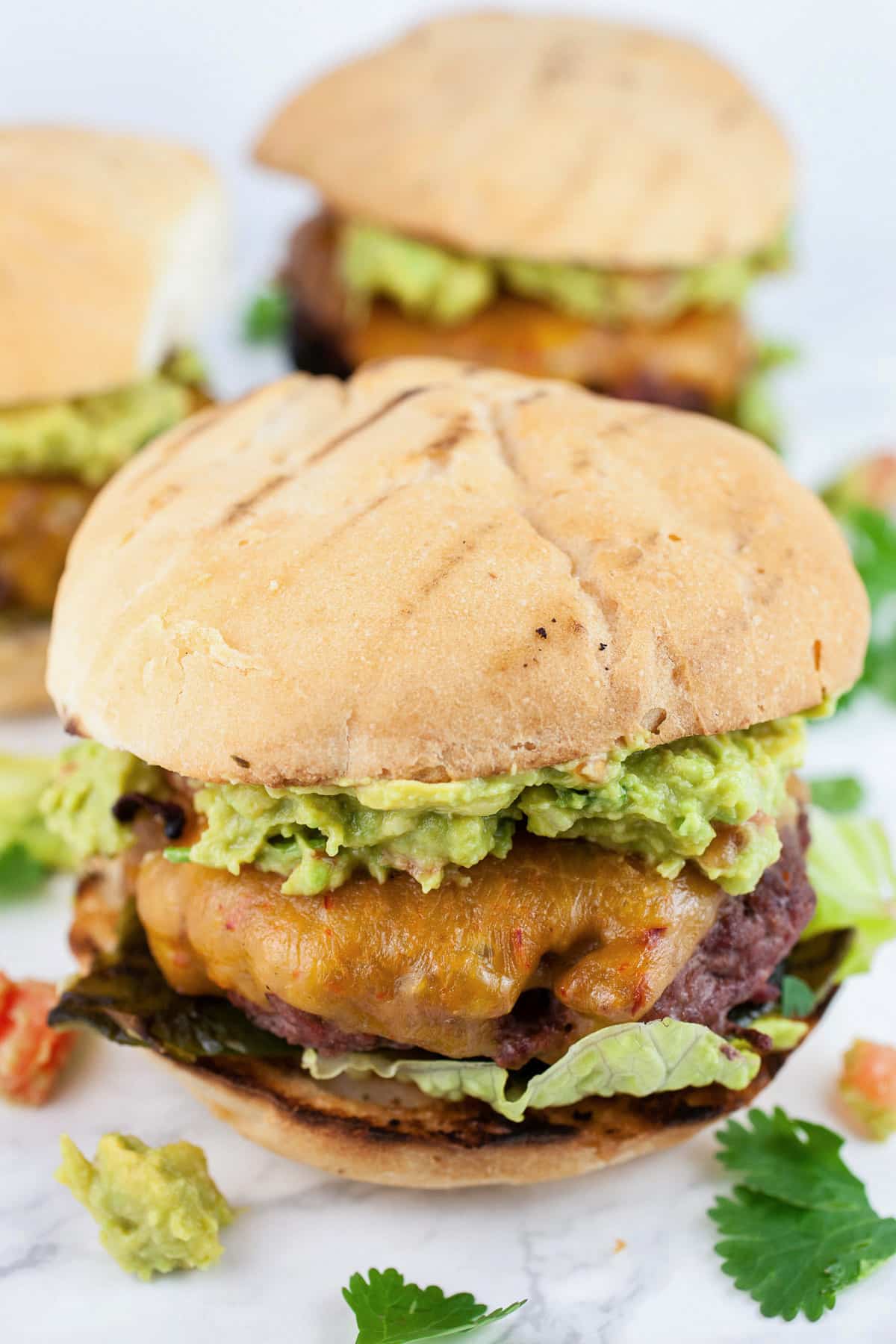 These Guacamole and Roasted Poblano Burgers are juicy and cooked to perfection on the grill! The beef is sprinkled with a light seasoning and grilled to perfection. The toppings include roasted poblano peppers and the best homemade guacamole. They're a little smoky and a little spicy. These gourmet burgers have a Southwest kick! #burgers #grill #southwest #poblano #guacamole #beef Southwest poblano burgers with guacamole and cilantro.