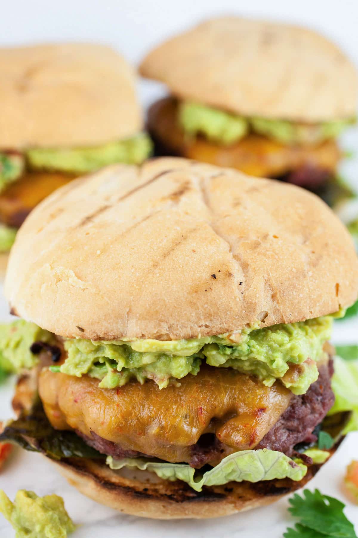 These Guacamole and Roasted Poblano Burgers are juicy and cooked to perfection on the grill! The beef is sprinkled with a light seasoning and grilled to perfection. The toppings include roasted poblano peppers and the best homemade guacamole. They're a little smoky and a little spicy. These gourmet burgers have a Southwest kick! #burgers #grill #southwest #poblano #guacamole #beef Southwest burgers with roasted poblanos, avocado guacamole, and cilantro.