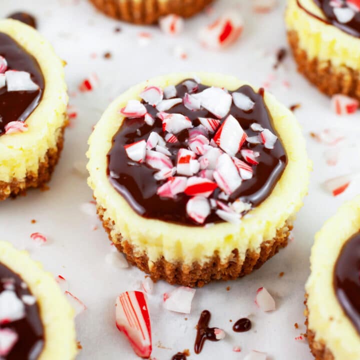 Peppermint cheesecake cups topped with chocolate ganache and crushed candy canes.