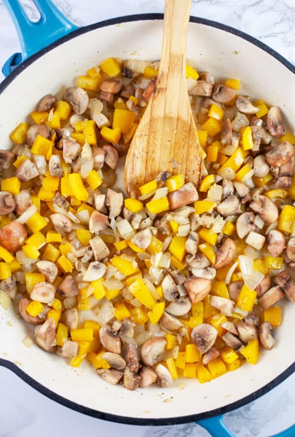 Diced mushrooms and yellow bell peppers in skillet with wooden spoon.