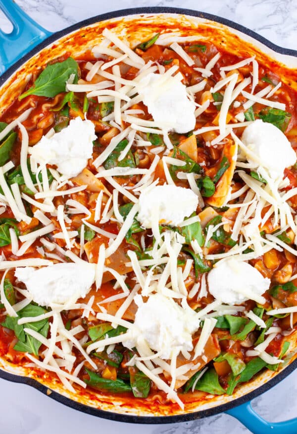 Vegetable lasagna topped with ricotta and grated mozzarella cheese in skillet.