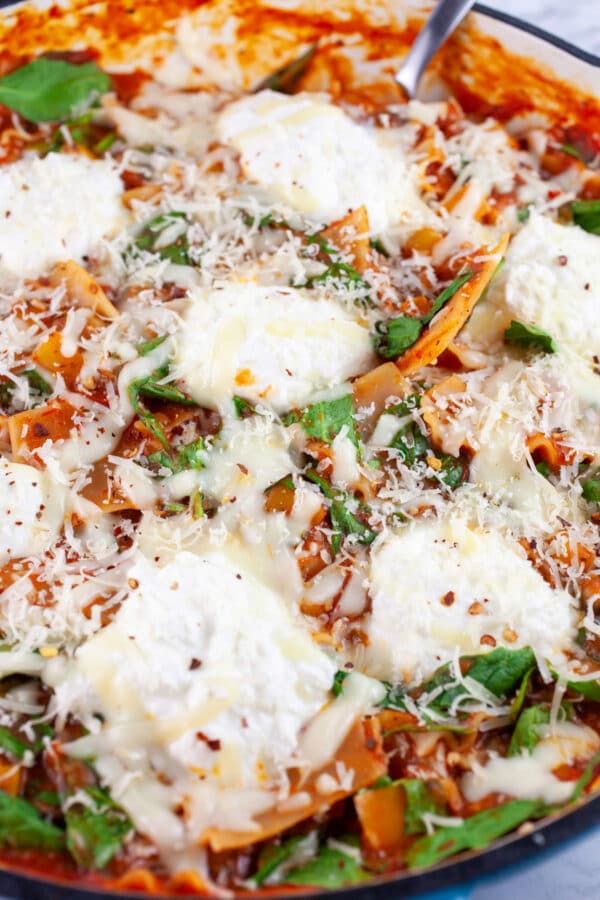 Cooked vegetable lasagna in skillet with metal spoon.