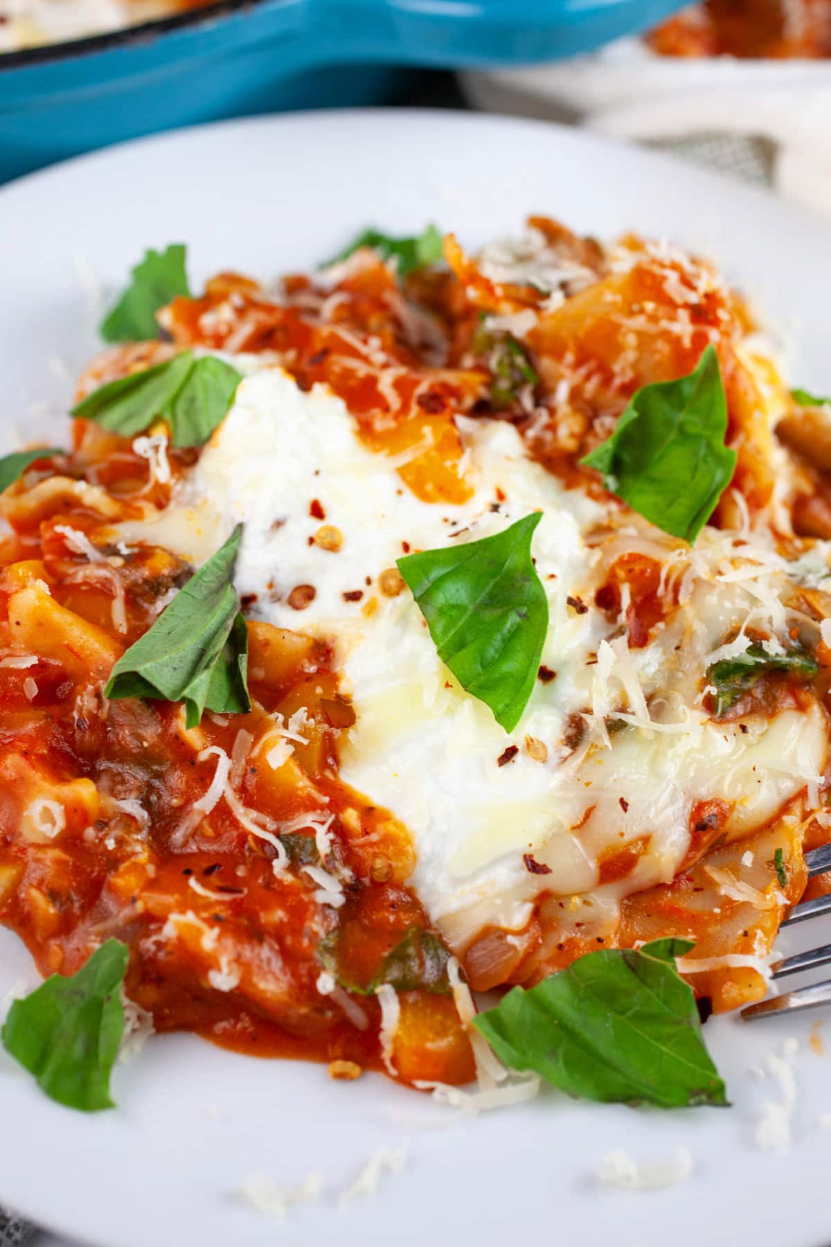This Cheesy Skillet Vegetable Lasagna recipe is the perfect one pan one pot meal! It's hearty and easy to make. It's got spinach, mushrooms, noodles, and ricotta cheese. This vegetarian weeknight dinner is one of the best healthy comfort foods out there! It's great for the winter and summer months. #lasagna #vegetablelasagna #vegetarian #pasta #cheesy #skillet Skillet vegetable lasagna garnished with fresh basil on white plate with fork.
