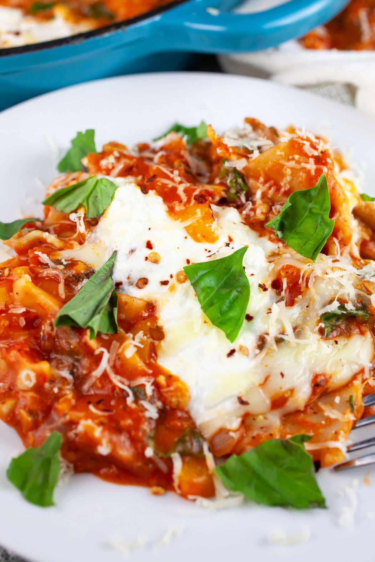This Cheesy Skillet Vegetable Lasagna recipe is the perfect one pan one pot meal! It's hearty and easy to make. It's got spinach, mushrooms, noodles, and ricotta cheese. This vegetarian weeknight dinner is one of the best healthy comfort foods out there! It's great for the winter and summer months. #lasagna #vegetablelasagna #vegetarian #pasta #cheesy #skillet Skillet vegetable lasagna garnished with fresh basil on white plate.