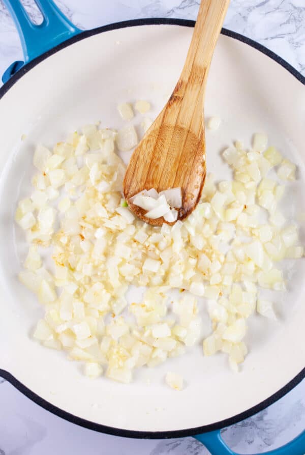 Minced garlic and onions in skillet with wooden spoon.
