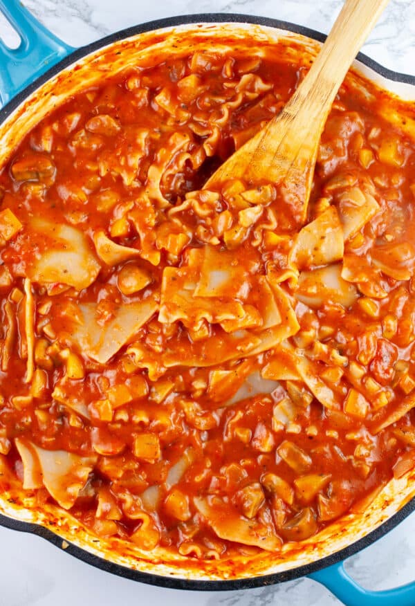 Lasagna noodles cooked in marinara sauce in skillet with wooden spoon.