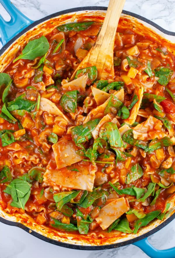 Lasagna noodles and spinach cooked in marinara sauce in skillet with wooden spoon.