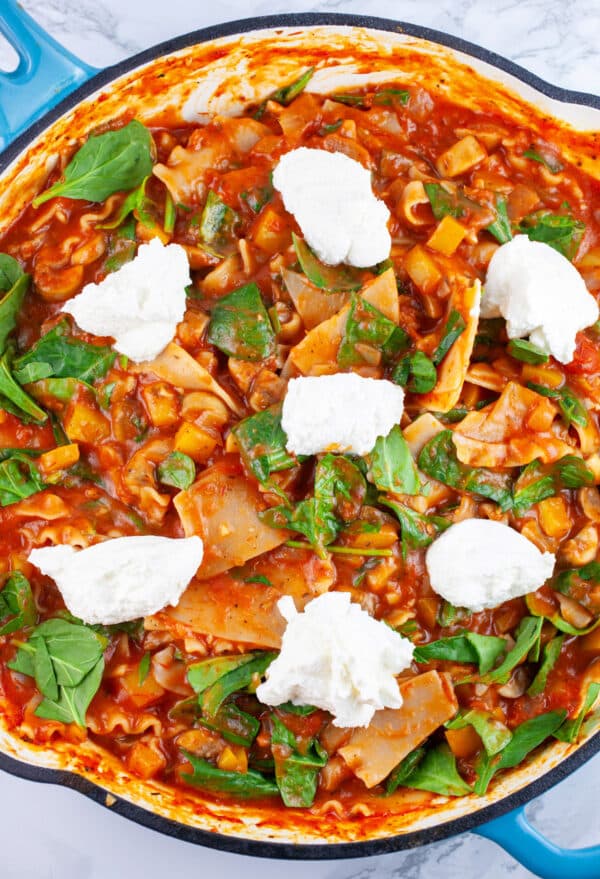 Cooked lasagna dotted with ricotta cheese in skillet.