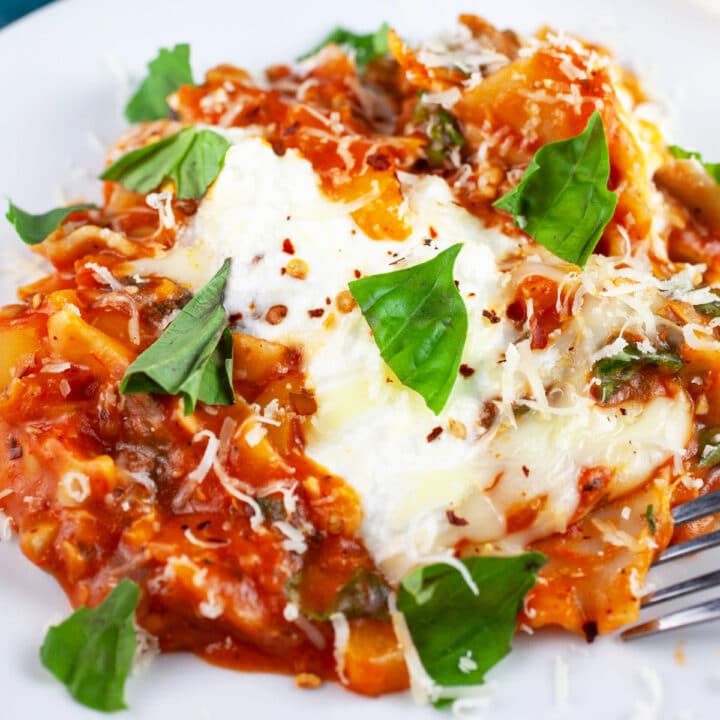 Skillet vegetable lasagna garnished with fresh basil on white plate.