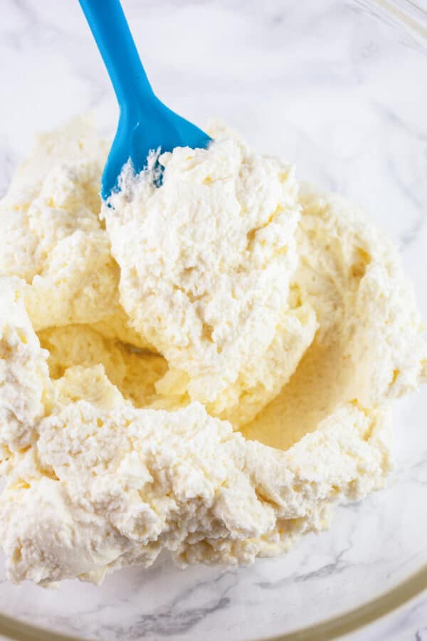 Blue spatula lifting whipped mascarpone cream from glass bowl.