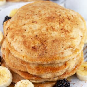 Stack of banana cinnamon pancakes on white plate with fork.