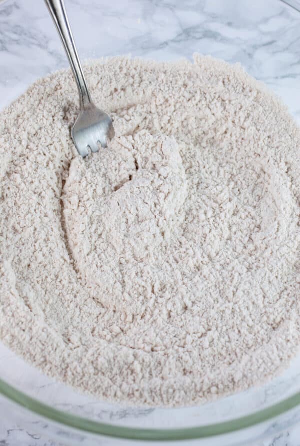 Dry ingredients in glass mixing bowl with fork.