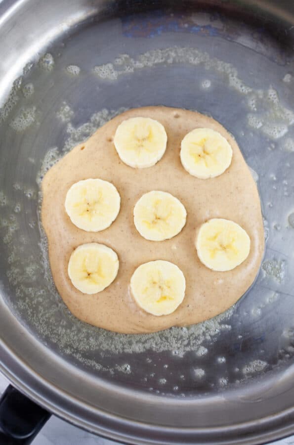Uncooked pancake with banana slices in skillet.