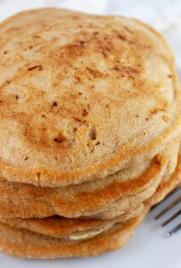 Stack of banana pancakes on white plate with fork.