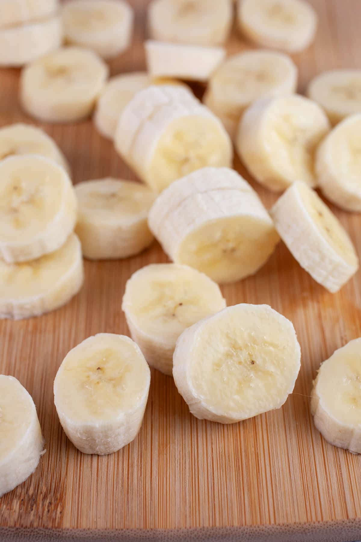 These Old-Fashioned Banana Pancakes are the perfect breakfast for weekday mornings or a weekend treat! They're light and fluffy, easy to make, and fun to eat. This simple pancake recipe is adapted from an old church cookbook. These banana pancakes are made from scratch and topped with maple syrup. Homemade is always best! #ad @kempscows #pancakes #banana #oldfashioned Sliced bananas on wooden cutting board.