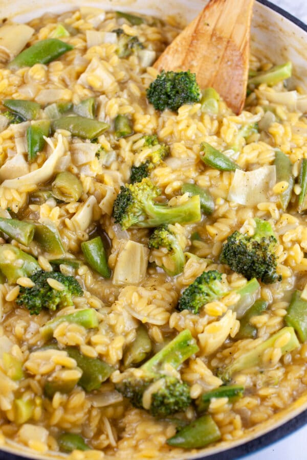 Vegetable pesto pasta with wooden spoon in skillet.