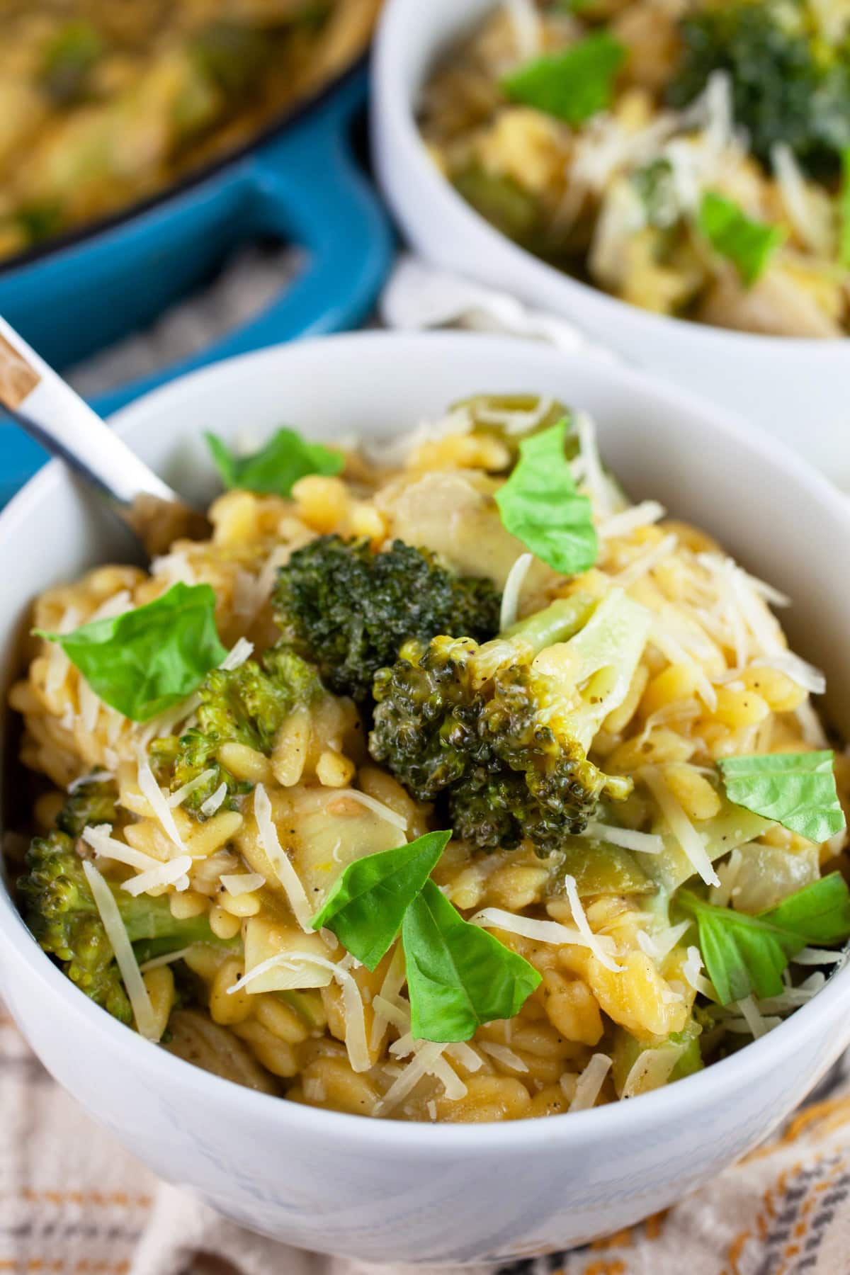Vegetable pasta with broccoli and snap peas garnished with fresh basil in white bowls.