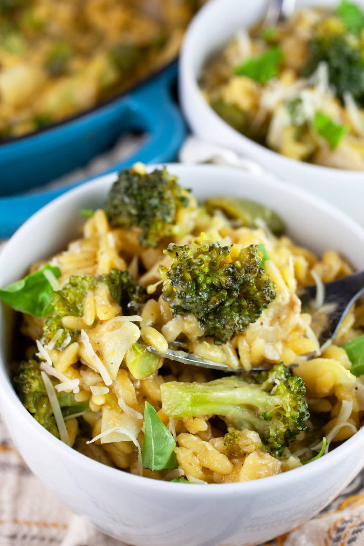 Vegetable pesto pasta with broccoli and peas in white bowls garnished with fresh basil.