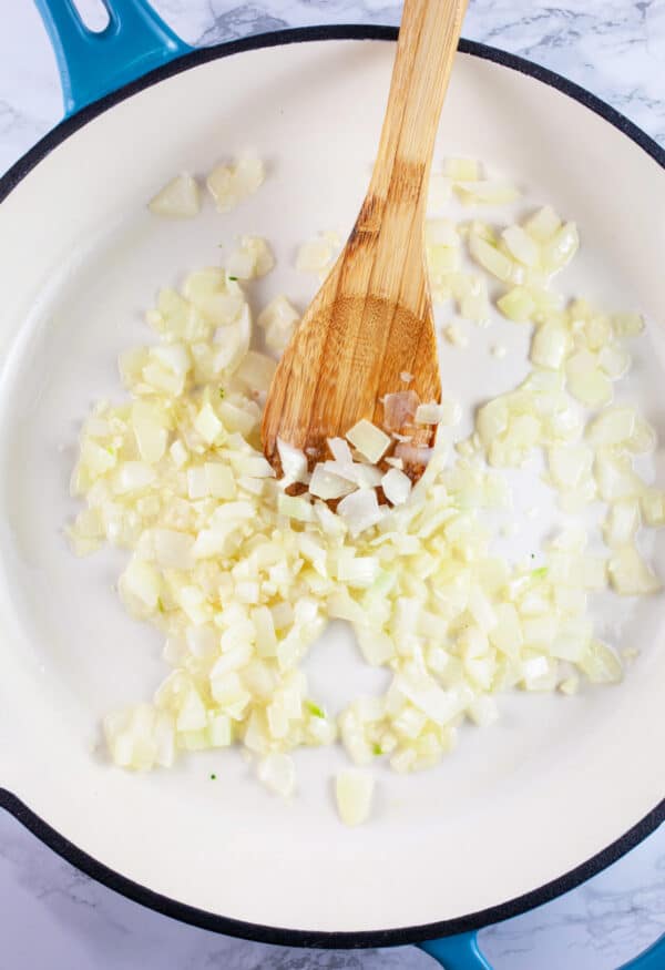 Minced garlic and onions sauteed in skillet with wooden spoon.