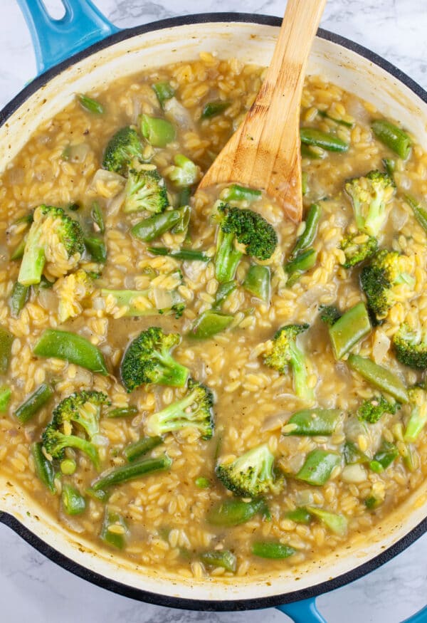Cooked vegetable orzo pasta in skillet with wooden spoon.