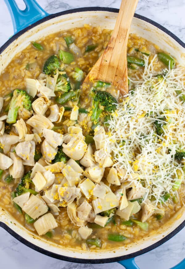 Vegetable pasta with marinated artichokes and Parmesan cheese in skillet with wooden spoon.