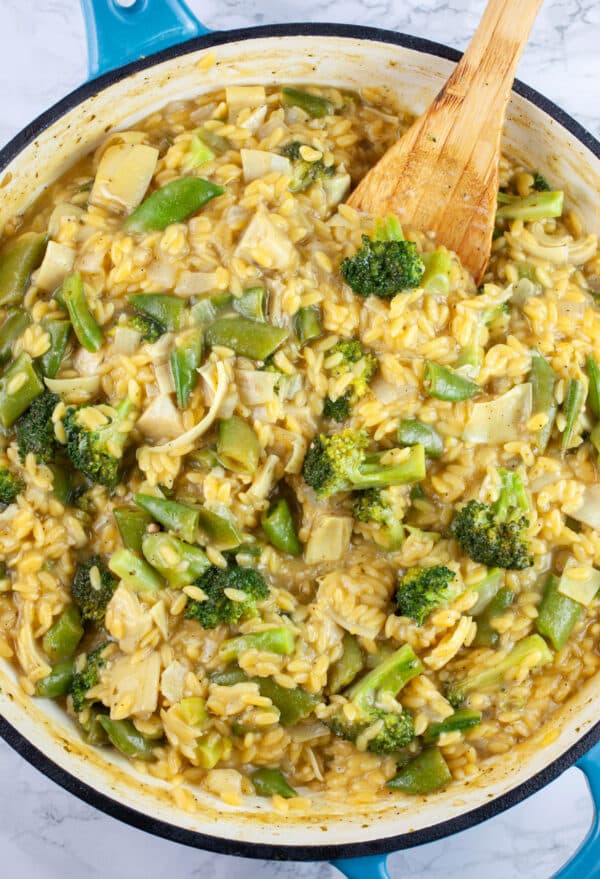 Cooked pesto vegetable pasta in skillet with wooden spoon.