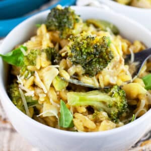 Vegetable pesto pasta garnished with fresh basil in white bowl with fork.