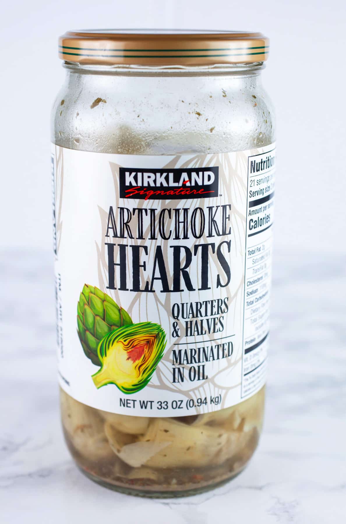 Jar of marinated artichoke hearts on white surface.