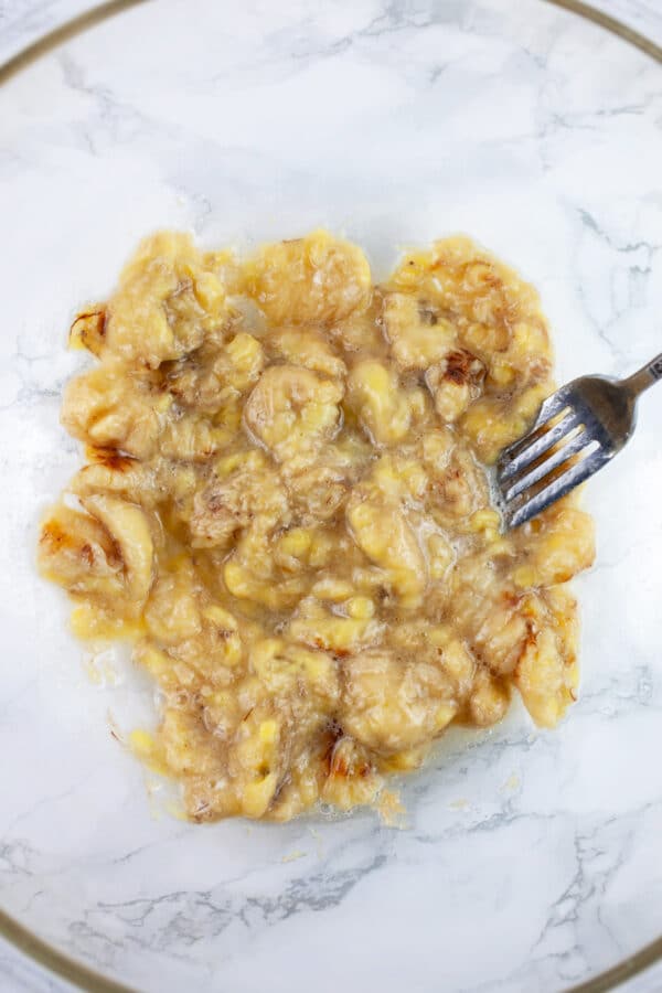 Mashed roasted bananas in glass bowl with fork.