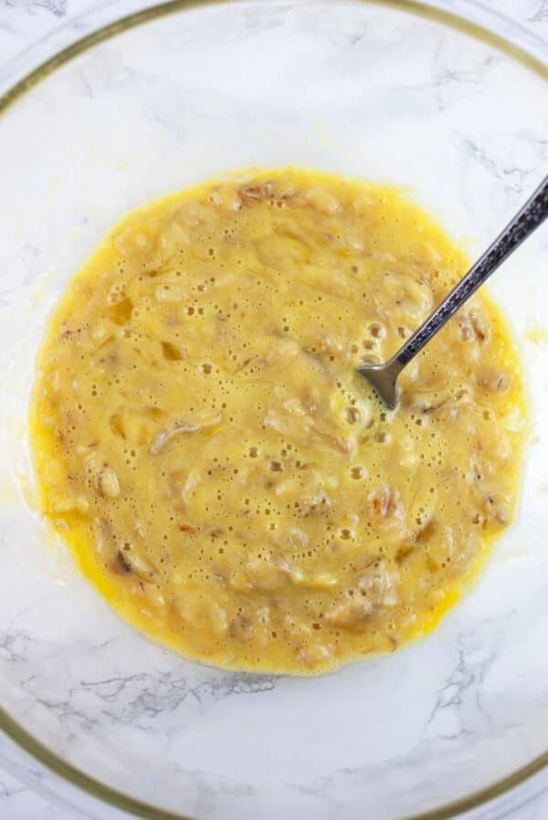 Egg and banana mixture in glass bowl with fork.