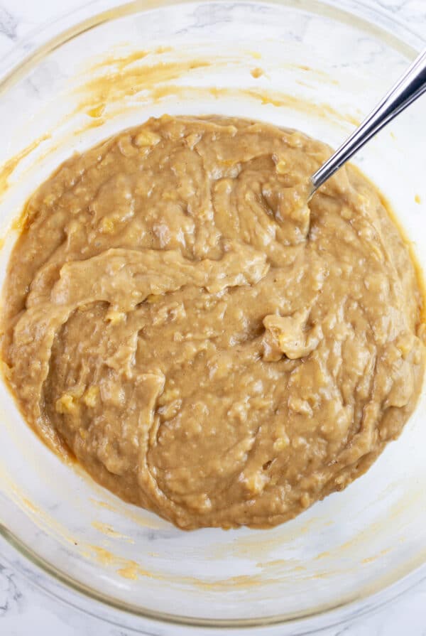 Banana muffin batter combined in glass mixing bowl with fork.