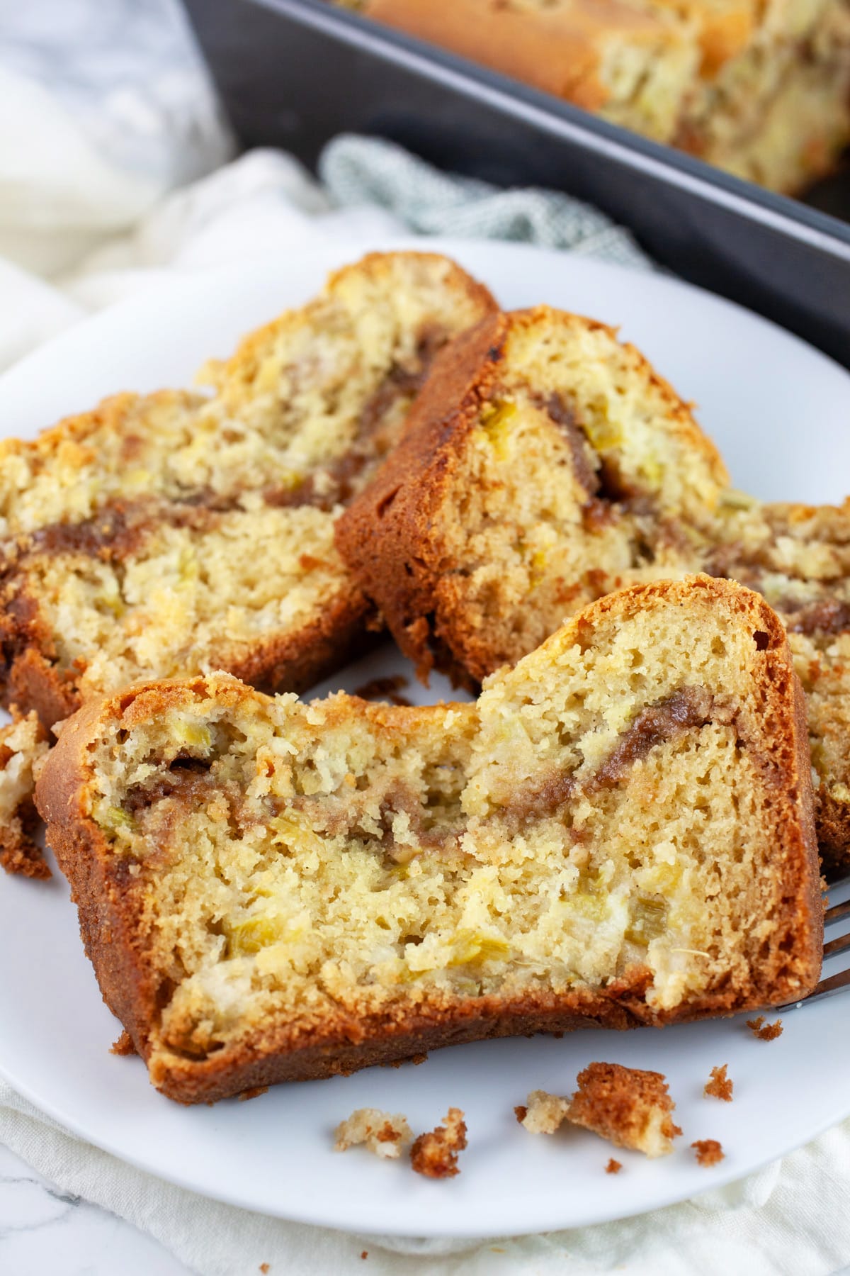 This Old Fashioned Rhubarb Bread is easy to make and totally delicious! It's made with sour cream so it's super moist. A layer of cinnamon streusel is baked into the middle of the bread giving it great crunch and texture. Perfect for breakfast, brunch, or dessert! This recipe is gluten free as well. A great way to welcome the spring and summer season! #rhubarb #bread #breakfast #streusel #glutenfree Slices of gluten free rhubarb on white plate with fork.