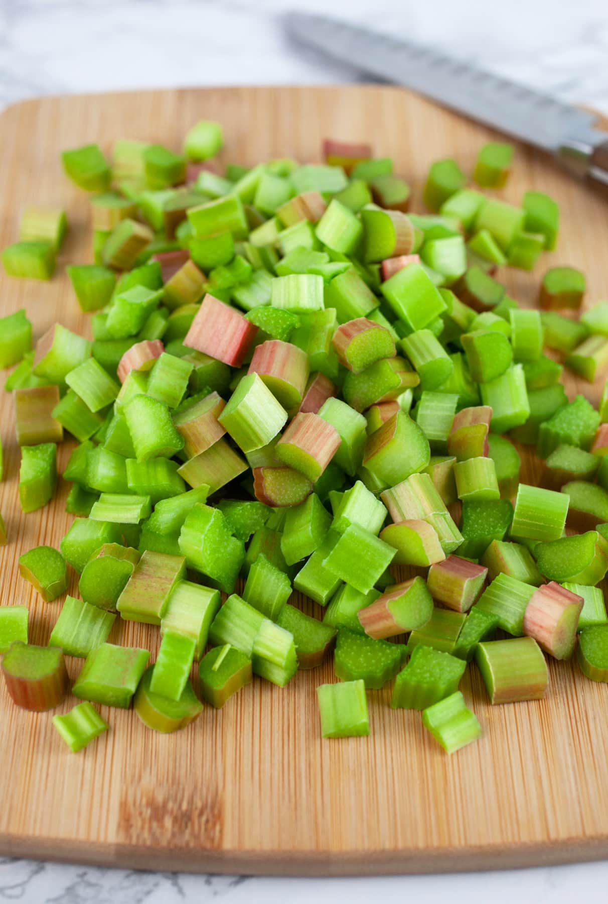 Diced rhubarb on wooden cutting board with knife.