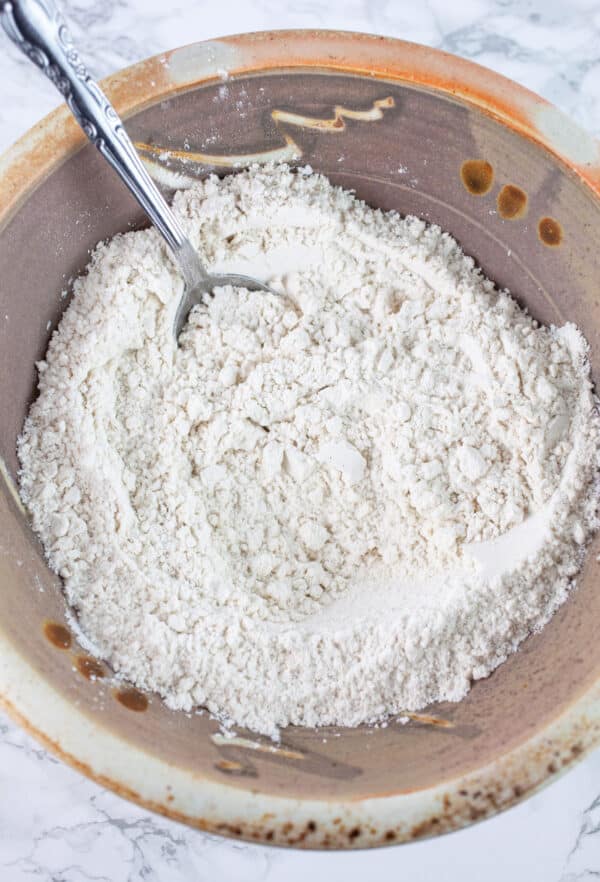 Dry ingredients in ceramic bowl with metal spoon.