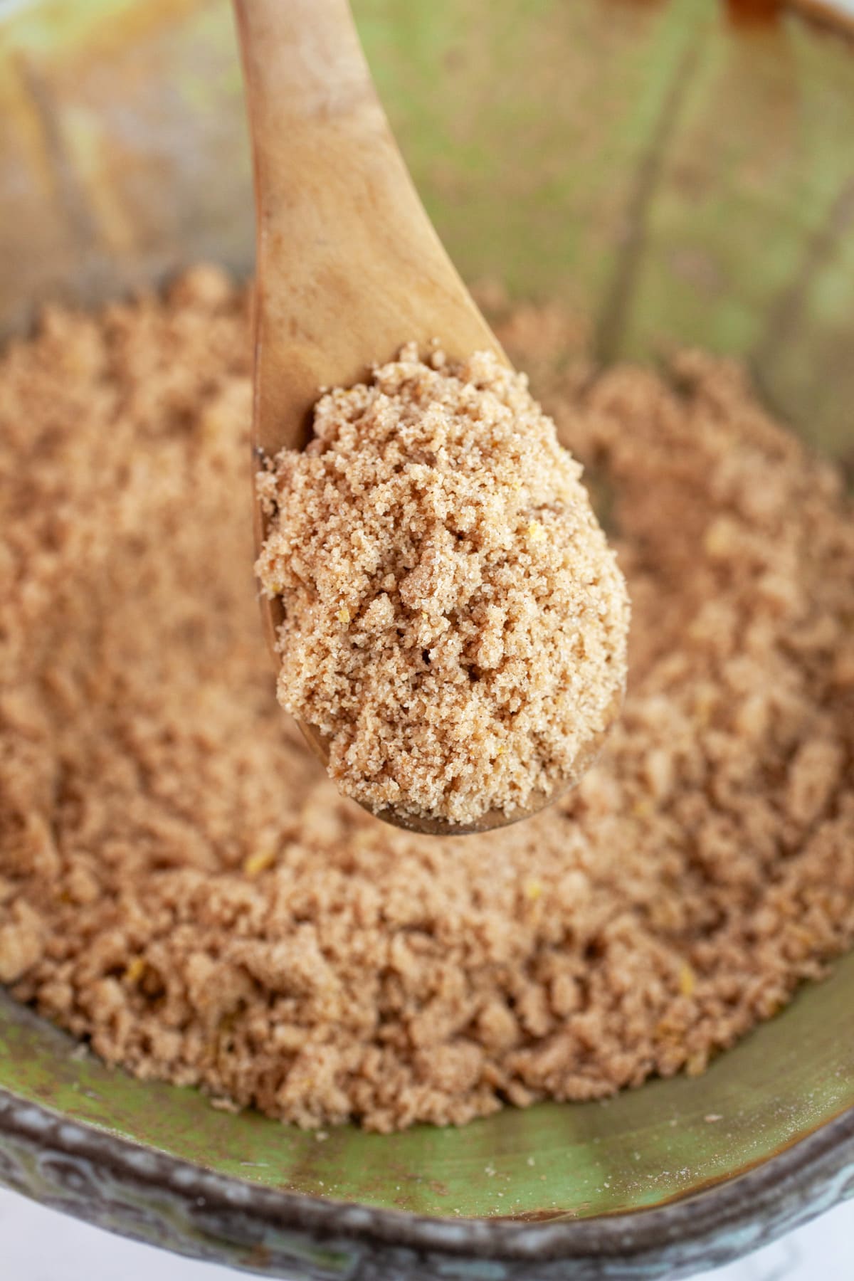 Wooden spoonful of streusel lifted from ceramic bowl.