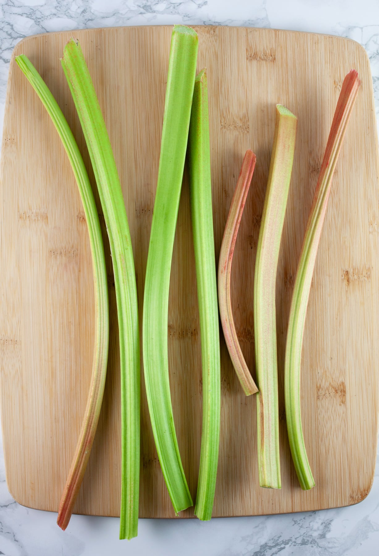 Stalks of rhubarb on wooden cutting board.