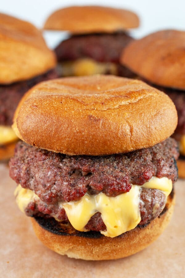 Grilled burger on bun with cheese melting out of the sides on wooden serving board.