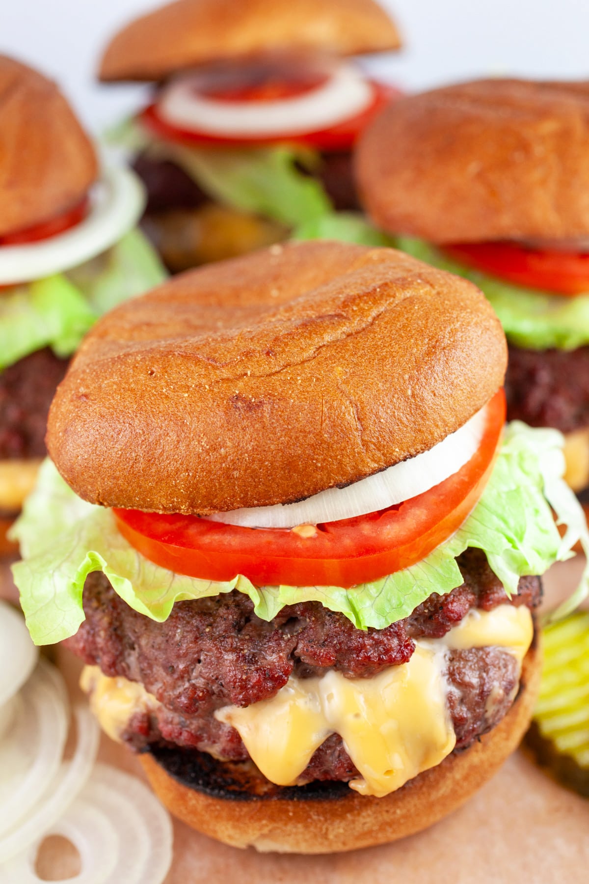 Grilled Juicy Lucy burgers with lettuce, tomato, onion, and pickles on wooden serving board.