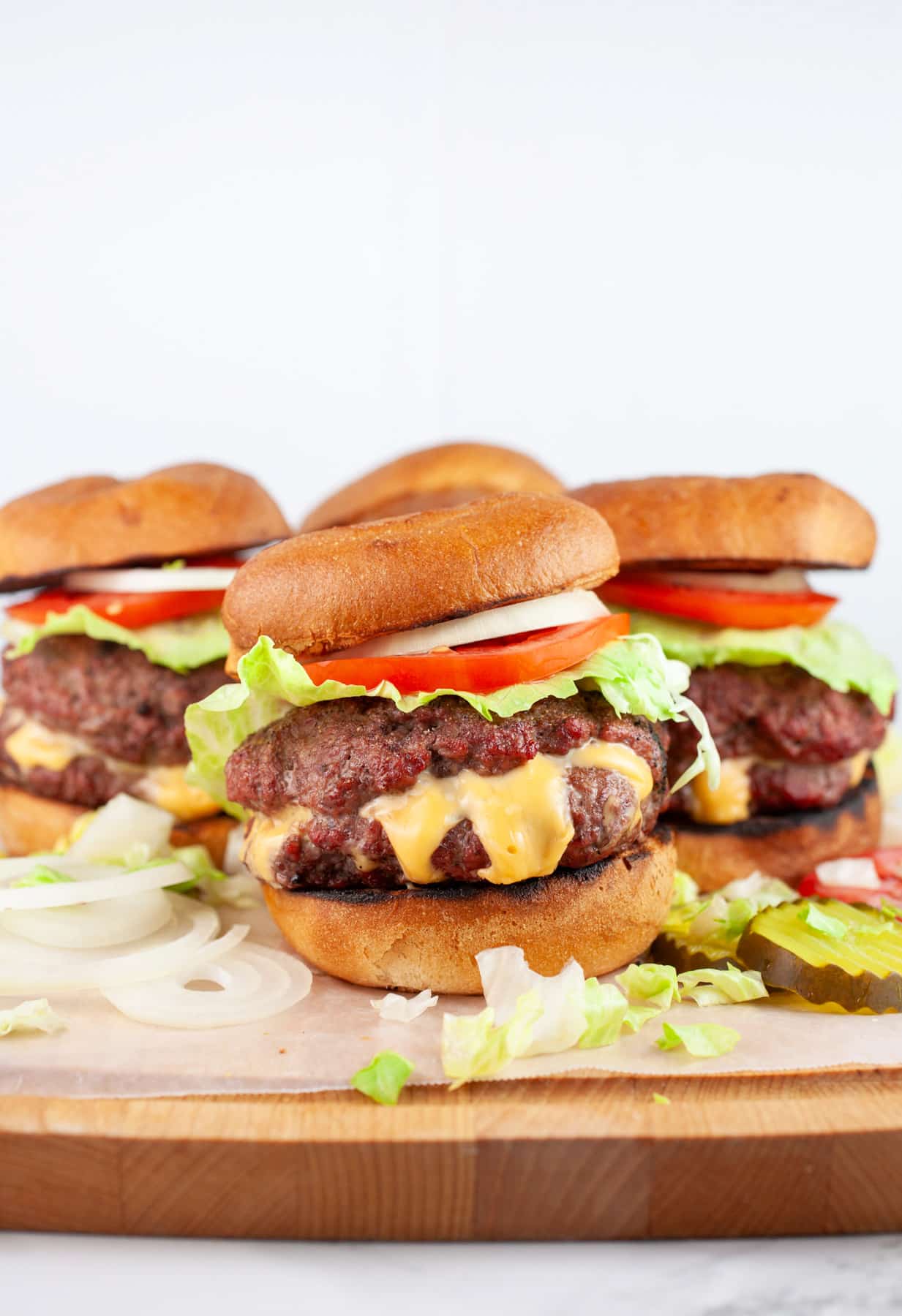 Juicy Lucy burgers with toppings on wooden serving board.
