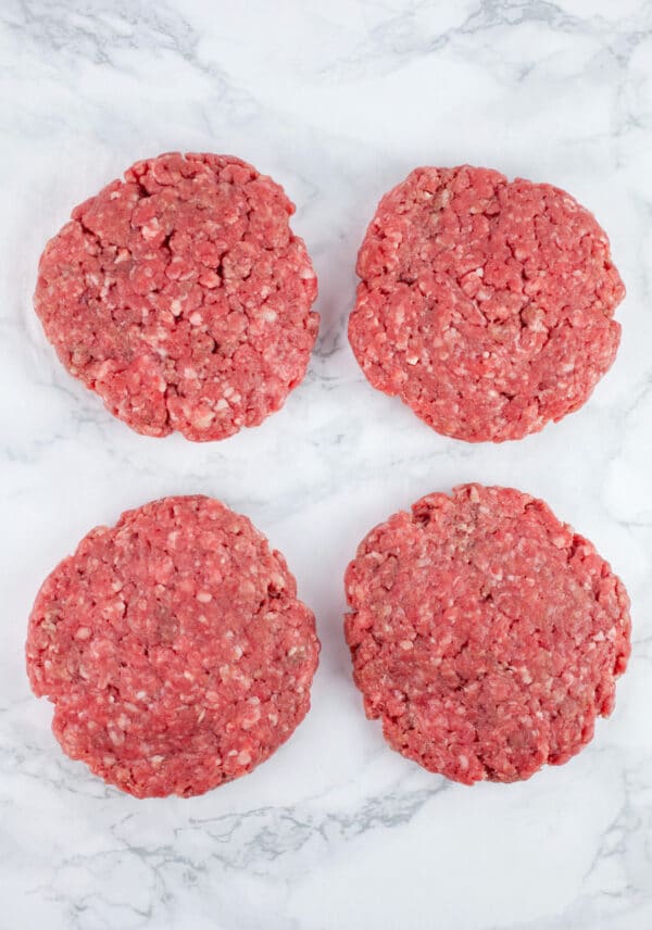 Raw beef patties on white surface.