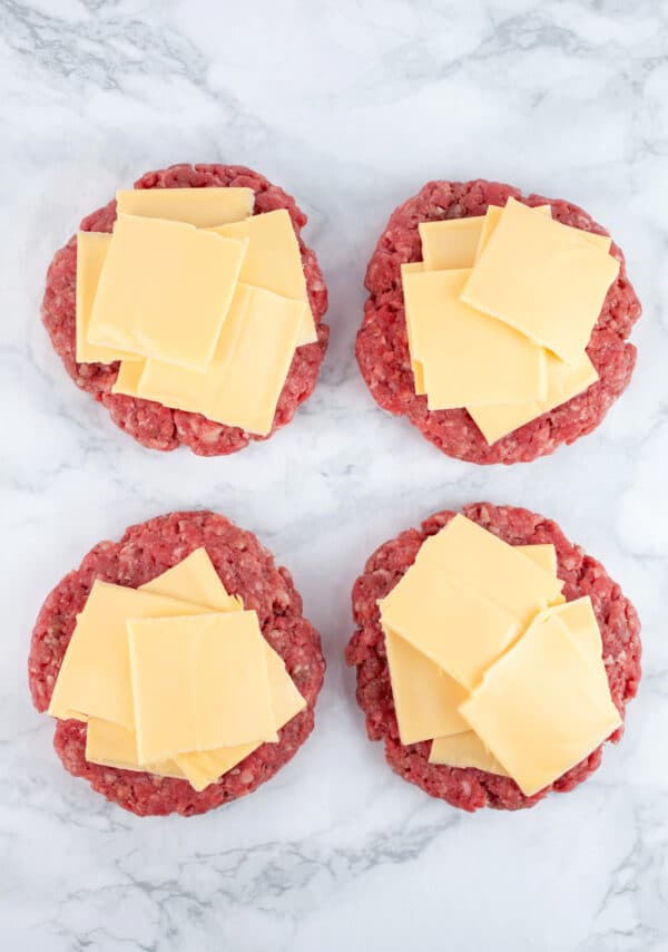 Raw beef patties topped with pieces of American cheese.